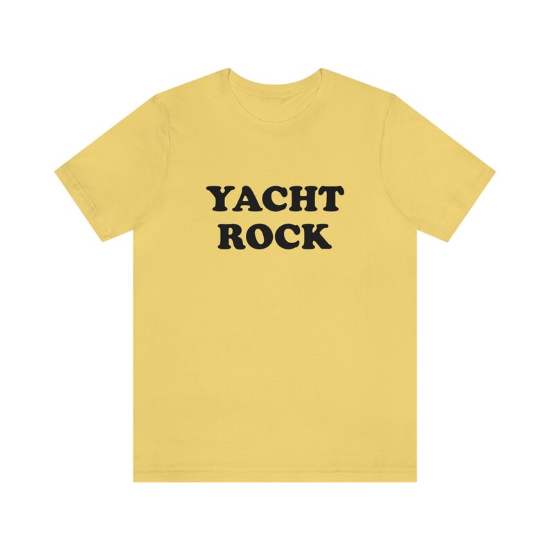 Puede incluir: Una camiseta amarilla con el texto "YACHT ROCK" impreso en negro.