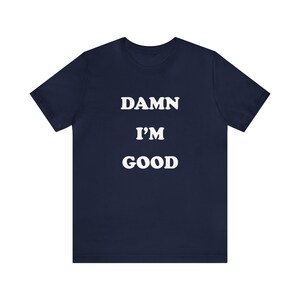 May include: Navy blue t-shirt with white text that reads "DAMN I'M GOOD".
