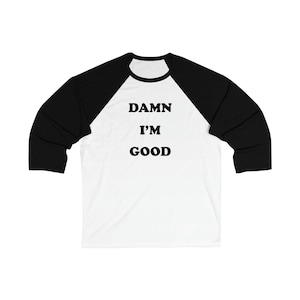 May include: White and black baseball tee shirt with the text "DAMN I'M GOOD" printed on the front.