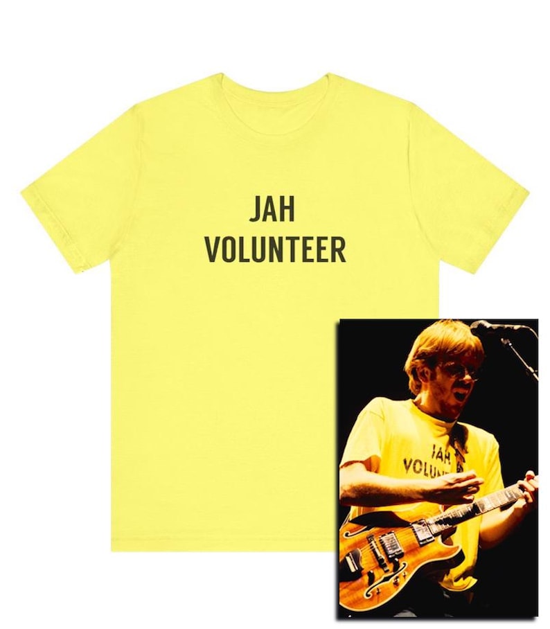 May include: Yellow t-shirt with the text "JAH VOLUNTEER" printed in black. A photo of a person wearing a similar t-shirt while playing a guitar is shown in the bottom right corner.