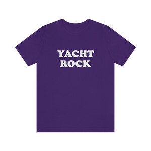 Puede incluir: Camiseta morada con el texto "YACHT ROCK" en blanco.