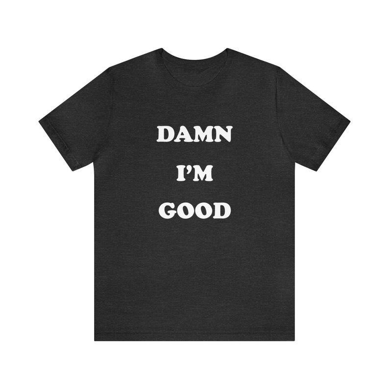 May include: A dark heather grey t-shirt with the text "DAMN I'M GOOD" printed in white.