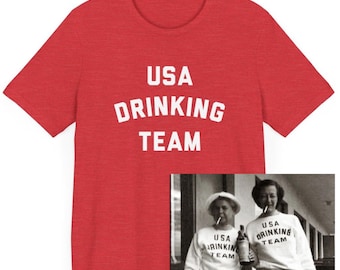 May include: Red t-shirt with the text "USA DRINKING TEAM" in white. The t-shirt is shown next to a black and white photo of two women wearing white sweatshirts with the same text.
