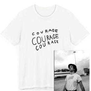 May include: White t-shirt with the word "COURAGE" written three times in black, with each word slightly different in style.