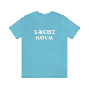 Puede incluir: Una camiseta azul claro con el texto "YACHT ROCK" impreso en blanco.