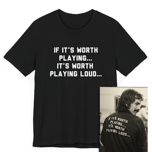 Pode incluir: Camiseta preta com texto branco que diz "If it's worth playing... it's worth playing loud..." O texto é repetido em uma foto preto e branco de uma pessoa vestindo a camiseta.