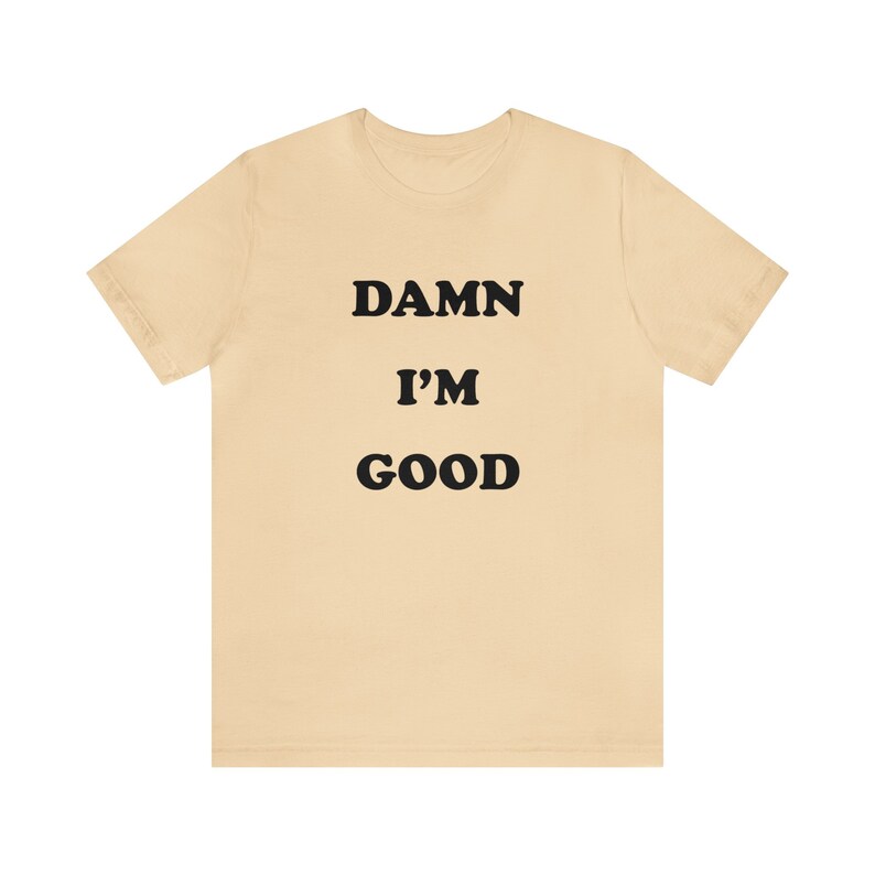 May include: A beige t-shirt with the text "DAMN I'M GOOD" printed in black.