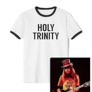 May include: White t-shirt with a black ringer and the text "HOLY TRINITY" printed in black. A photo of a man wearing a similar t-shirt with the text "HOLY TRINITY" is shown in the background.