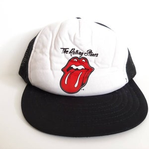 Puede incluir: Gorra de camionero blanca y negra con un logotipo de lengua roja y el texto "The Rolling Stones".