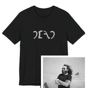May include: Black t-shirt with the word "DEAD" written in white on the front. The t-shirt is being worn by a person in a black and white photo. The person is wearing sunglasses and has a beard. The photo is taken outdoors.