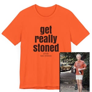 May include: Bright orange t-shirt with the text "get really stoned" and "drink wet cement" in black. The shirt is short-sleeved and has a crew neck. A smaller image shows a person wearing the shirt.