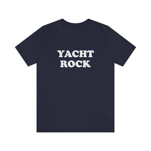 Puede incluir: Una camiseta azul marino con el texto "YACHT ROCK" impreso en blanco.