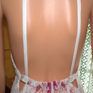 Peut inclure: Robe d'&eacute;t&eacute; blanche avec un motif floral rouge et rose. La robe pr&eacute;sente un dos nu avec des bretelles blanches et une taille d&eacute;corative. Les bretelles sont attach&eacute;es &agrave; la robe dans le dos.