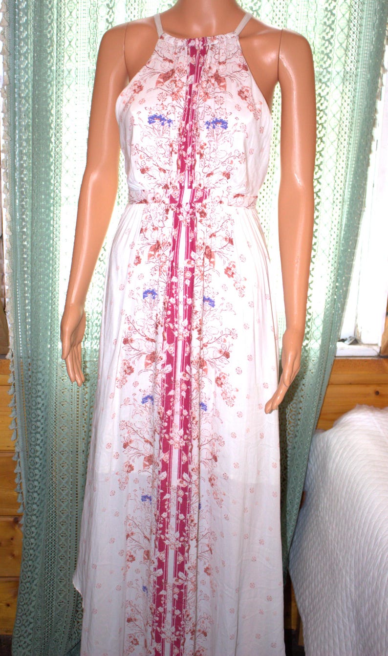Peut inclure: Robe blanche &agrave; col licou avec un motif floral dans les tons de rouge, marron et bleu. La robe pr&eacute;sente une bande verticale de tissu magenta au centre et une taille cintr&eacute;e. La robe est longue.
