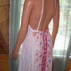 Peut inclure: Robe blanche sans dos avec imprim&eacute; floral. La robe pr&eacute;sente un col halter et une jupe pliss&eacute;e avec un panneau vertical de tissu bordeaux et floral. La robe est faite d'un tissu l&eacute;ger.