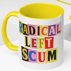 May include: White ceramic mug with a yellow interior and handle. The mug features the text "RADICAL LEFT SCUM" in a colorful, cut-out letter style. The mug is on a white surface with yellow accents.