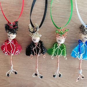 Puede incluir: Cuatro collares de muñeca de vidrio envueltos en alambre con vidrio y alambre de diferentes colores. Las muñecas tienen el pelo negro, los ojos marrones y llevan vestidos de alambre y cuentas.