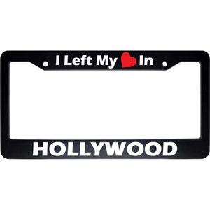 May include: Black license plate frame with white text that reads "I Left My Heart In HOLLYWOOD". A red heart symbol is between the words "My" and "In".