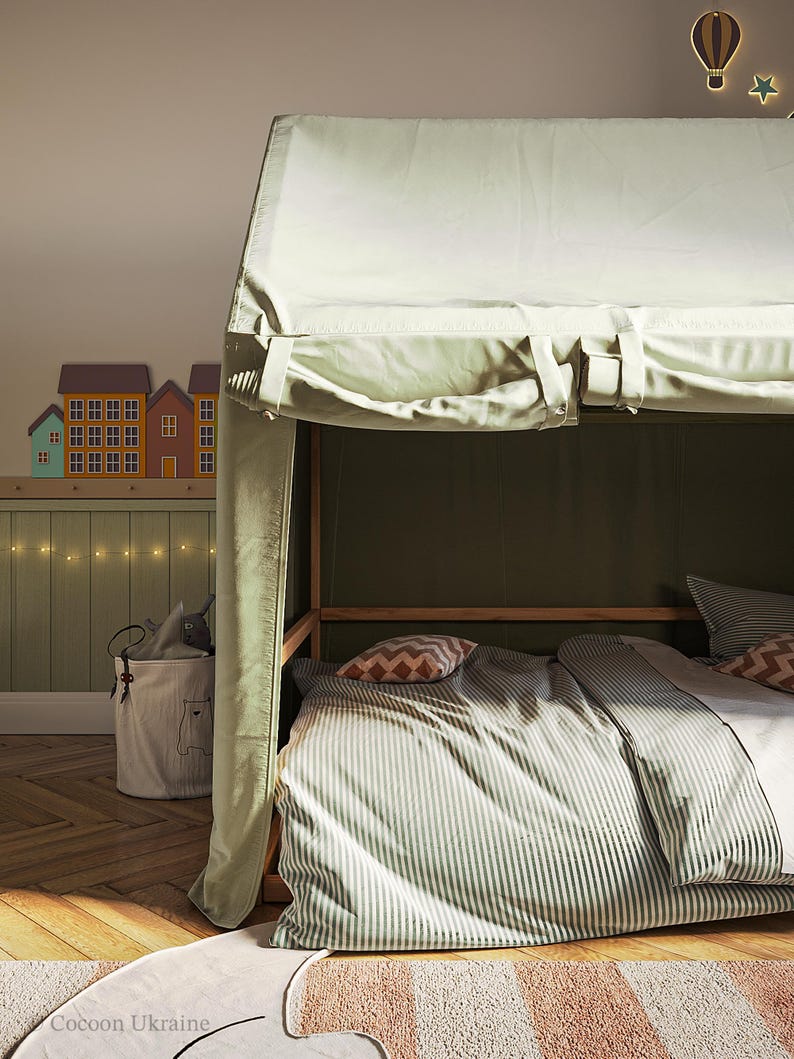 Puede incluir: Un edred&oacute;n a rayas verdes y blancas con un dosel blanco sobre la cama. La cama est&aacute; en una habitaci&oacute;n con suelo de madera y una pared verde. Hay luces de cadena en la pared y una peque&ntilde;a cesta con un animal de peluche dentro.
