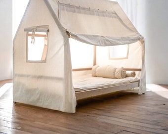May include: A white canvas tent-like structure with a wooden frame, designed to fit over a bed. The tent has a small window and a rolled-up fabric flap. The bed is made of wood and has a white mattress and a white pillow.