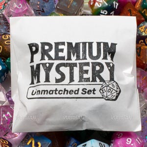 May include: A white paper bag with the words "PREMIUM MYSTERY Unmatched Set" in black text is surrounded by a variety of colorful polyhedral dice. The dice are in various colors and materials, including clear, glittery, and opaque.
