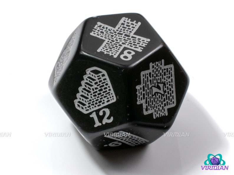 Op de afbeelding: Zwarte 12-zijdige dobbelsteen met witte nummers en symbolen. De dobbelsteen heeft een nummer 12, een nummer 8 en een symbool van een muur met een trap.