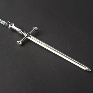 May include: A silver sword pendant necklace with a chain. The sword has a cross guard and a pointed tip.