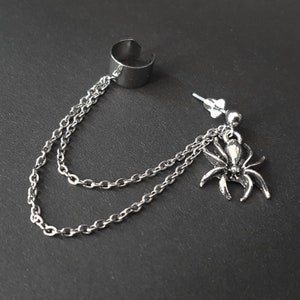 Puede incluir: Un pendiente de aro de plata con un colgante de araña que cuelga de una cadena de plata.