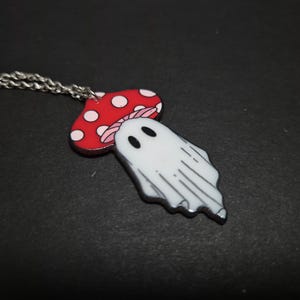 Può includere: Una collana con catena d'argento con un ciondolo a forma di fungo rosso e bianco con un fantasma bianco che emerge dalla parte superiore.
