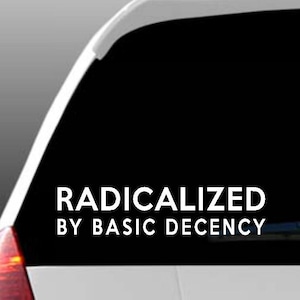 May include: A white car window with a black background. The text "RADICALIZED BY BASIC DECENCY" is displayed in white. The car's taillight is visible on the left side of the image.