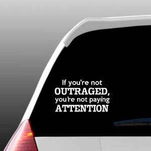May include: A white vinyl sticker with the text "If you're not OUTRAGED, you're not paying ATTENTION" on a black background. The sticker is on the back window of a car.