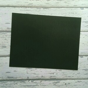 May include: A dark green piece of paper on a white wooden background.