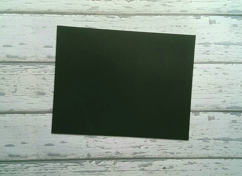 May include: A dark green piece of paper on a white wooden background.