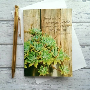 May include: A card with a wood background and a succulent plant. The card has a quote from Hebrews 7:25: "Jesus is able to save completely those who come to God through Him."