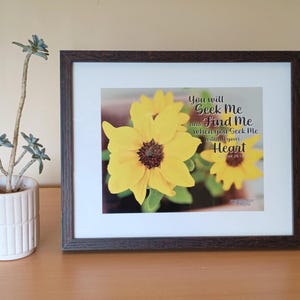 May include: A framed print showing bright yellow sunflowers with brown centres. The print includes the text "You will Seek Me and Find Me when you Seek Me with all your Heart". The frame is dark brown.