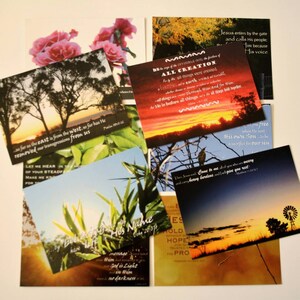 May include: A collection of inspirational postcards with religious quotes and nature scenes. The postcards feature a variety of colors, including pink, green, blue, and brown. The text on the postcards includes verses from the Bible, such as "As far as the east is from the west, so far has He removed our transgressions from us." and "Come to me, all you who are weary and carry heavy burdens, and I will give you rest."