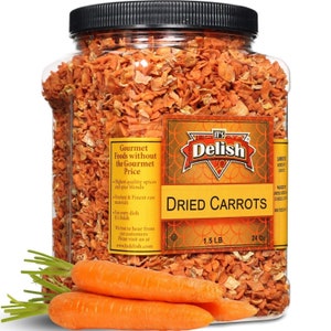 May include: A clear plastic jar filled with dried orange carrot pieces. The jar has a gold label with the text "It's Delish" and "Dried Carrots". The label also states "1.5 LB" and "24 Oz". Two whole orange carrots are in the foreground.
