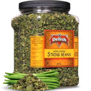 May include: A clear plastic jar filled with dried chopped string beans. The jar has a yellow and orange label that reads "It's Delish" and "Dried Chopped String Beans". The label also includes the text "Gourmet Foods without the Gourmet Price". A bunch of fresh green string beans are in the foreground.