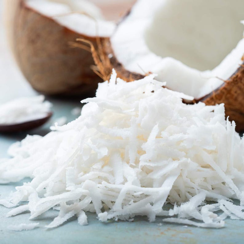May include: A close-up of a pile of unsweetened shredded coconut, a popular ingredient in baking and cooking. The coconut is white and fluffy, and it is piled high on a light blue surface.