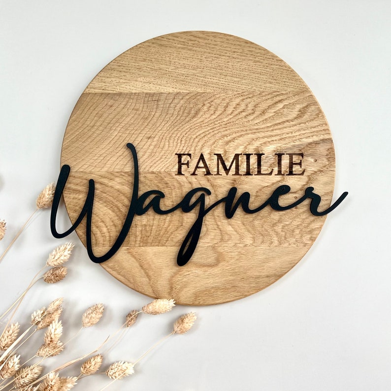 Rundes Holzschild ausEiche. In Großbuchstaben wird das Wort "FAMILIE"eingraviert. Der Wunschname bzw. Nachname wird als schwarzer 3D Text auf das Holz geklebt.