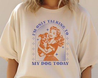 May include: A white t-shirt with a retro-style graphic of a woman holding a puppy. The graphic says "I'm only talking to my dog today".