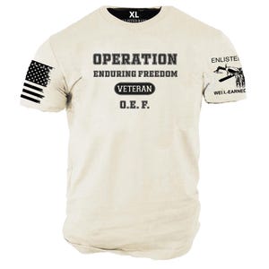 May include: Cream-colored t-shirt with the text "OPERATION ENDURING FREEDOM VETERAN O.E.F." in black. Features an American flag on the left sleeve and the words "ENLISTED" and "WELL-EARNED" on the right sleeve. The shirt is size XL.