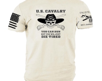 May include: Cream-colored t-shirt with a black graphic featuring a skull wearing a cowboy hat, crossed sabers, and the text "U.S. CAVALRY." The shirt also displays the text "YOU CAN RUN BUT YOU WIL JUST DIE TIRED" and an American flag on the left sleeve.
