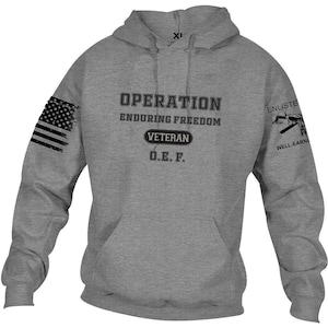 May include: A gray hooded sweatshirt with the words "OPERATION ENDURING FREEDOM VETERAN O.E.F." printed on the front. The left sleeve features a distressed American flag, and the right sleeve has a graphic and the words "ENLISTED WELL-EARNED."