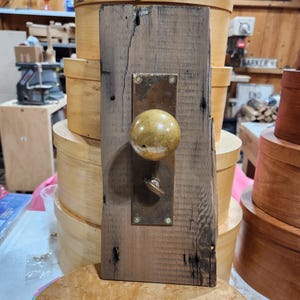 May include: A brass door knob with a keyhole and a decorative plate mounted on a weathered wooden plank.