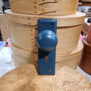 Op de afbeelding: Een donkerblauwe deurknop met een sleutelgat en een ronde knop. De knop is gemonteerd op een houten oppervlak.