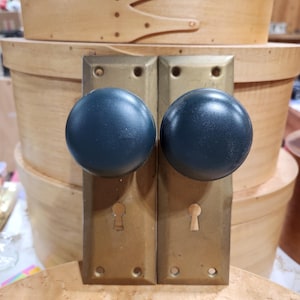 May include: A pair of antique brass door knobs with dark green porcelain handles. The knobs have a keyhole and are mounted on rectangular plates.