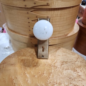 以下が含まれることがあります： 木製の箱に取り付けられた真鍮製の鍵穴とプレートが付いた白いセラミック製のドアノブ