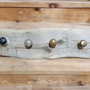 May include: A rustic wooden shelf with four knobs, one black and three brass, mounted on the surface. The shelf is made of weathered wood with a natural finish.