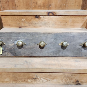 Peut inclure: Une planche en bois avec cinq boutons de porte en laiton antique. La planche est patinée et a un aspect rustique.